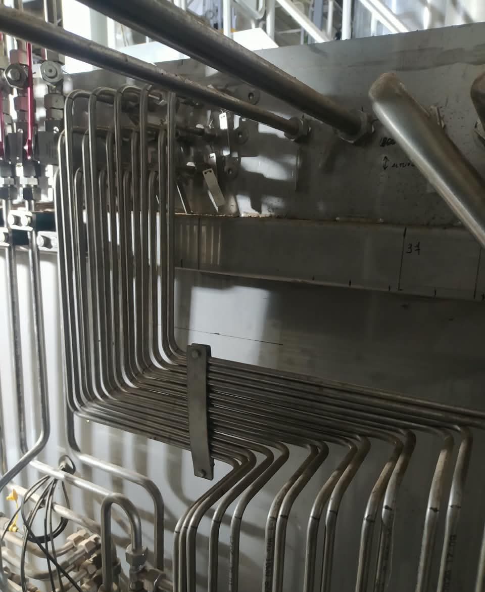 Feixe de tubos de aço inox dobrados em degrau, fixados numa parede metálica, em fábrica de celulose