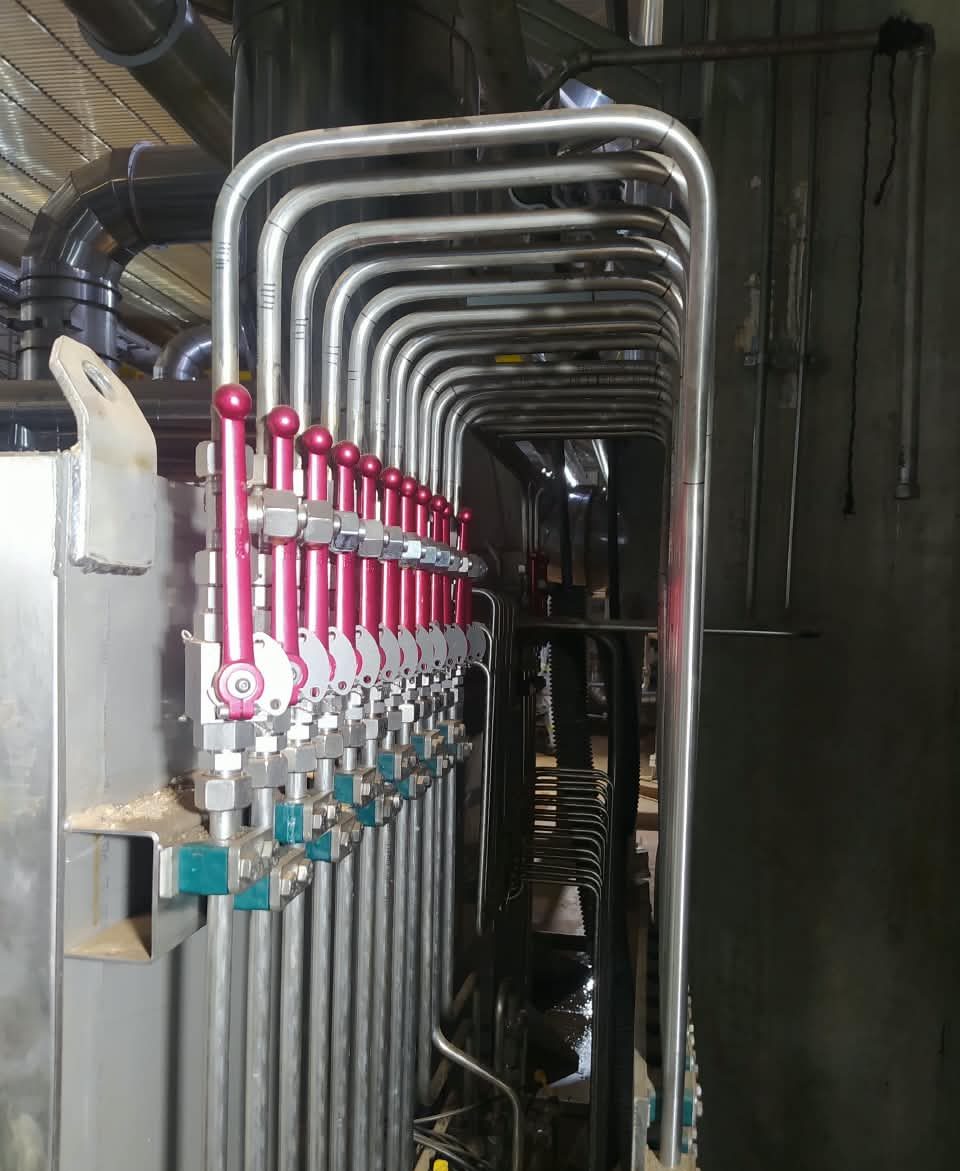 Tubos de aço inox curvados subindo por uma coluna e ligados a válvulas de manoplas vermelhas