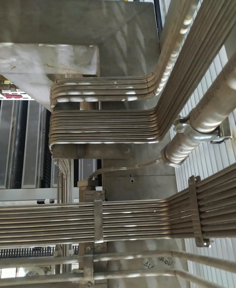 Feixes de tubos paralelos fixados e atravessando uma estrutura metálica, vistos de cima