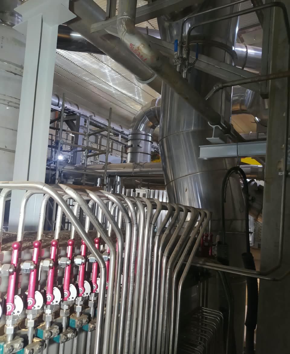 Válvulas de manoplas vermelhas e tubos de aço inox subindo ao lado de uma tubulação grande isolada