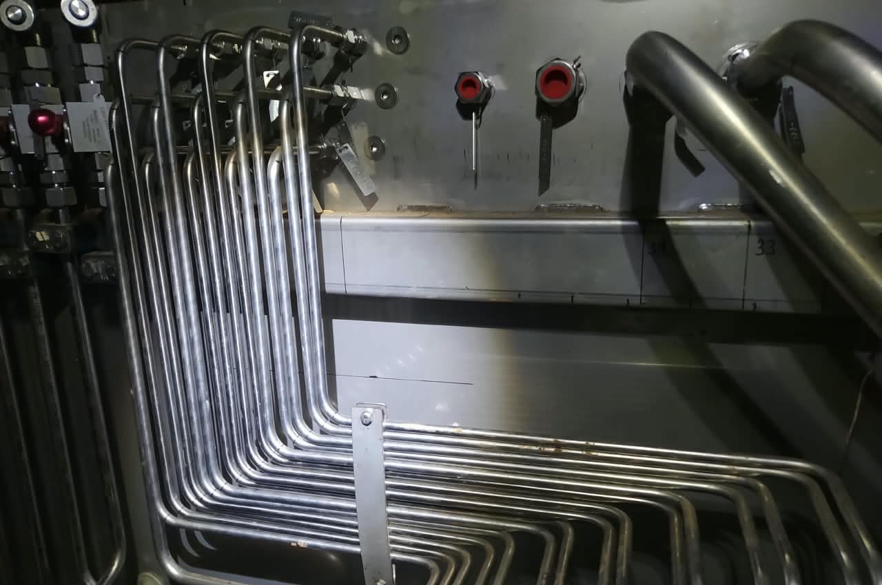Tubos de aço inox dobrados em ângulo sobre um painel, ao lado de dois botões vermelhos